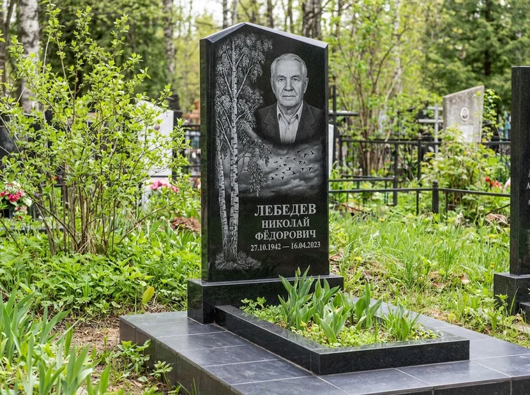 Памятник с гравировкой берёзы: вертикальная стела со скошенным верхом — берёза и стая птиц в небе, гранитный цоколь с тёмной плиткой, работа «Лебедев» в Нижневартовске