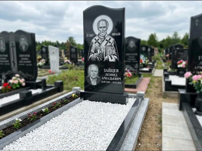 Памятник с гравировкой иконы: стела с крестообразным навершием — икона в резной рамке-киоте, газон без ограды, стриженая трава, работа «Раевская» в Нижневартовске