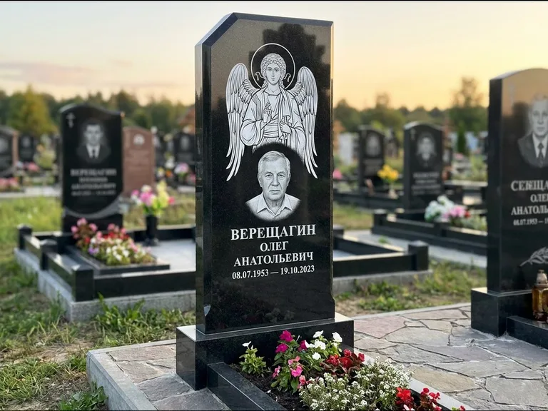 Памятник с гравировкой иконы: стела с резным навершием и нимбом в золоте — гравировка образа Спасителя, высокие разросшиеся туи полукругом, работа «Мельникова» в Нижневартовске