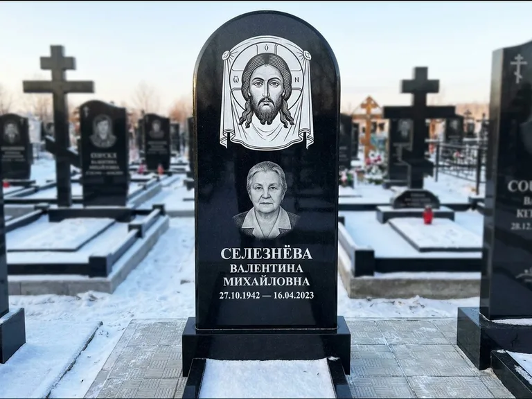 Памятник с гравировкой иконы: небольшая скромная одиночная стела с именной иконой — золочёный нимб на образе, аккуратный участок с газоном, работа «Ковалёв» в Нижневартовске