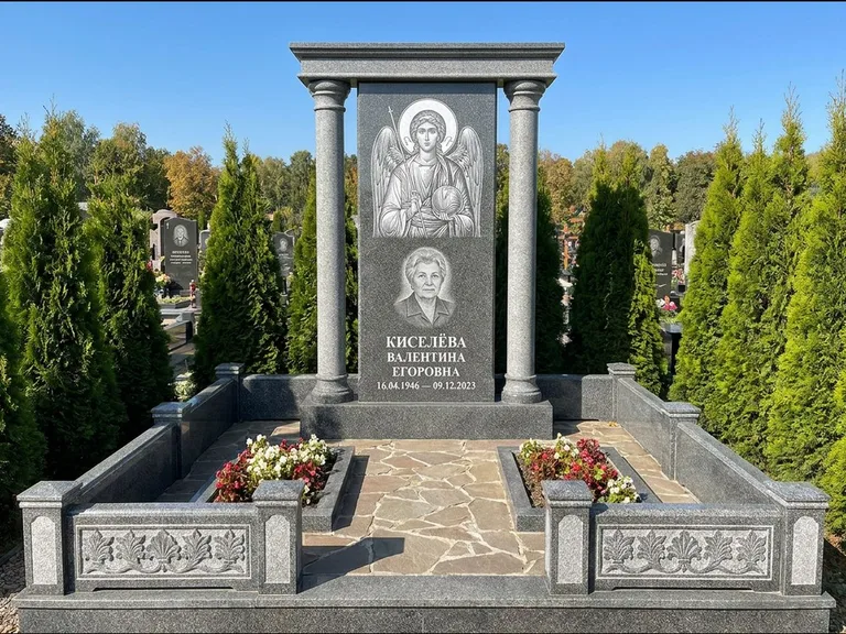Памятник с гравировкой иконы: массивная стела с двускатным навершием-домиком — гравировка Николая Чудотворца, живая изгородь из туи, работа «Журавлёв» в Нижневартовске