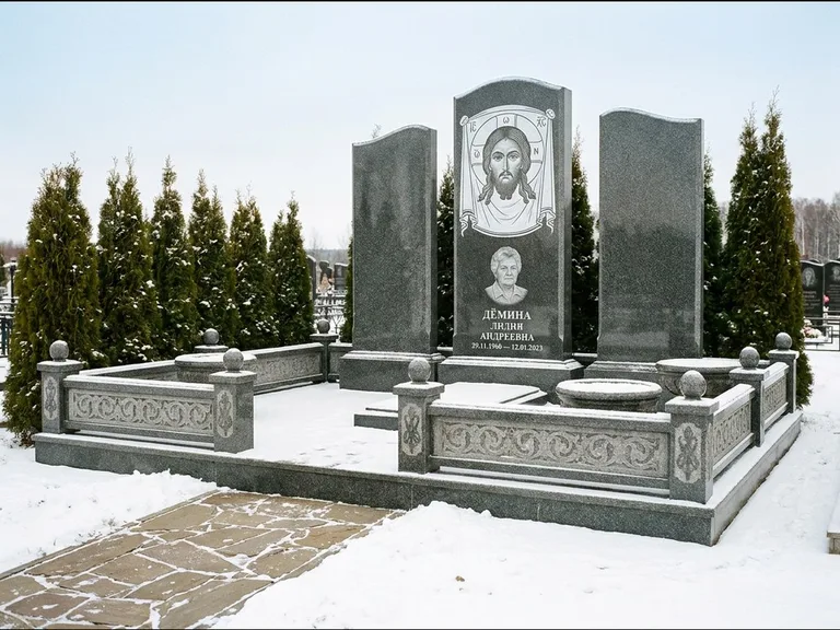 Памятник с гравировкой иконы: узкая вертикальная стела-пилон с ликом — икона в резной рамке-киоте, открытая лужайка без ограды, работа «Одинцов» в Нижневартовске