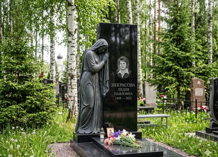 Гранитная фигура скорбящего мужчины у чёрной стелы в Нижневартовске